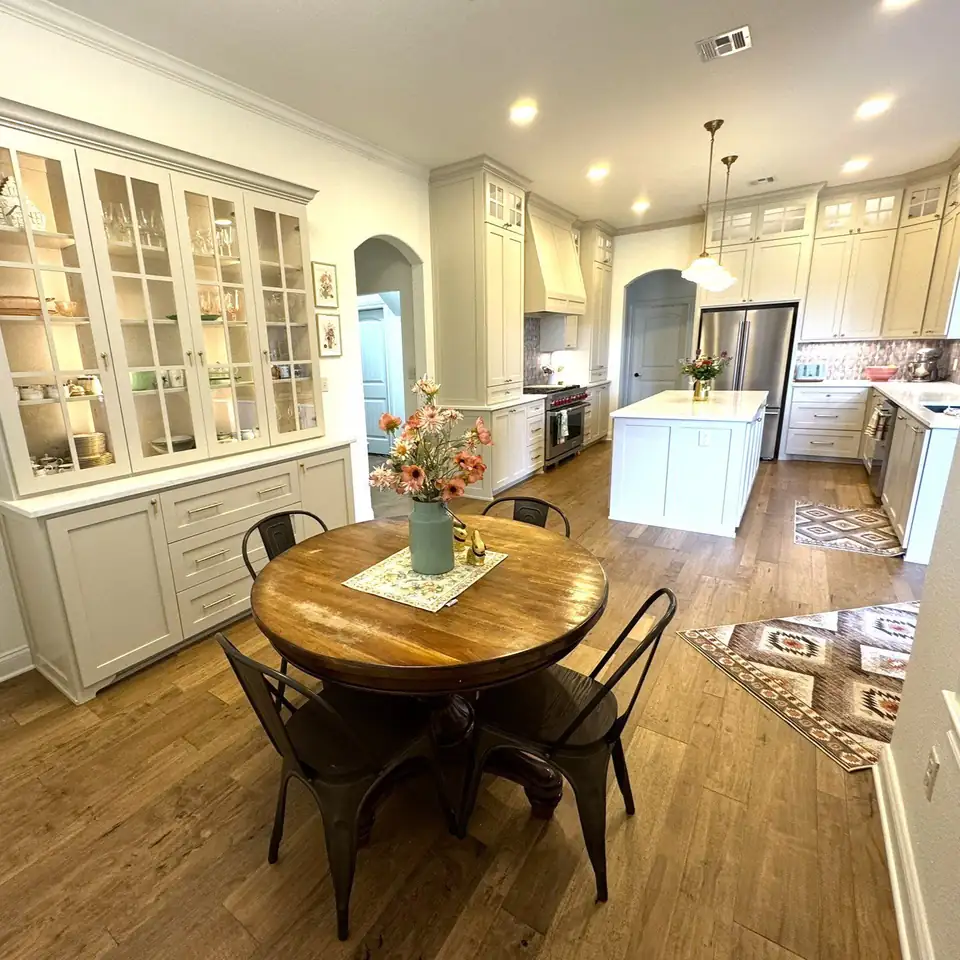 Open kitchen with cream shaker cabinets, white island, glass-front hutch and wood floors, a home remodeling project from a Waco remodeler
