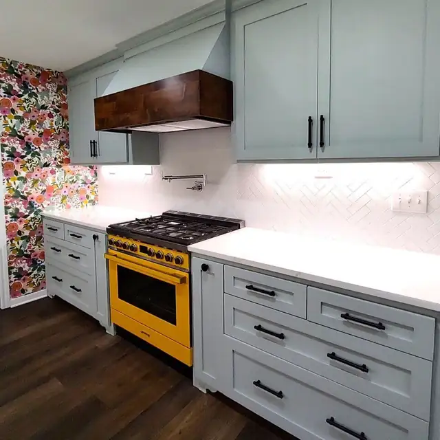 Sage green shaker cabinets with a walnut range hood, a yellow range and a white herringbone backsplash